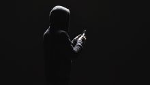 Dark photo of a man in a hoodie holding a phone to illustrate the article 