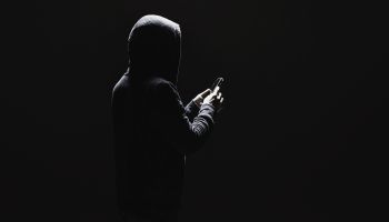 Dark photo of a man in a hoodie holding a phone to illustrate the article 