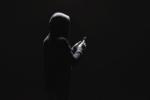 Dark photo of a man in a hoodie holding a phone to illustrate the article 