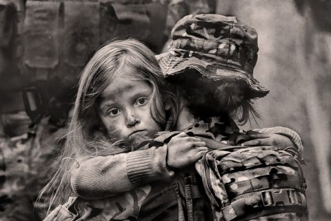 Photo of dazed young girl being carried by a soldier in a war setting to illustrate the article Why War?