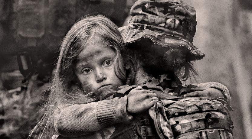 Photo of dazed young girl being carried by a soldier in a war setting to illustrate the article Why War?