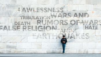 Person standing in front of a large wall displaying negative words associated with the end times, to illustrate the article 