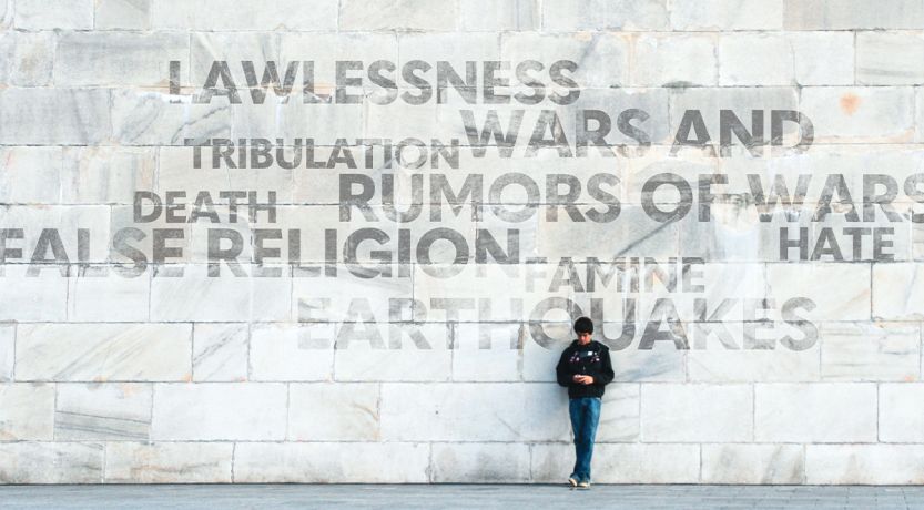 Person standing in front of a large wall displaying negative words associated with the end times, to illustrate the article 