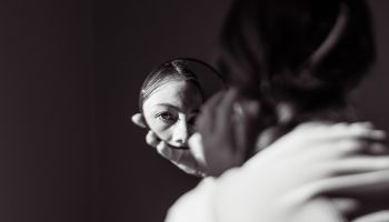 Dark photo of a girl's face reflected in a small round mirror to illustrate the article 