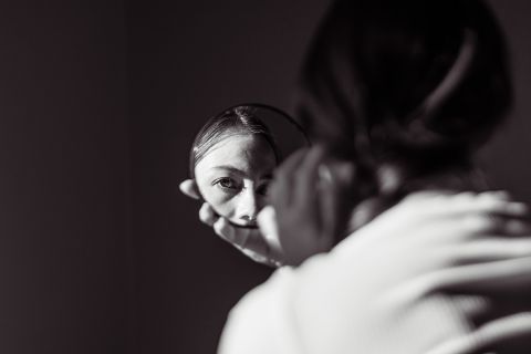 Dark photo of a girl's face reflected in a small round mirror to illustrate the article 