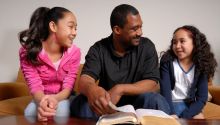 Photo of a father and two daughters with a Bible to illustrate the article Family Bible Study Topics