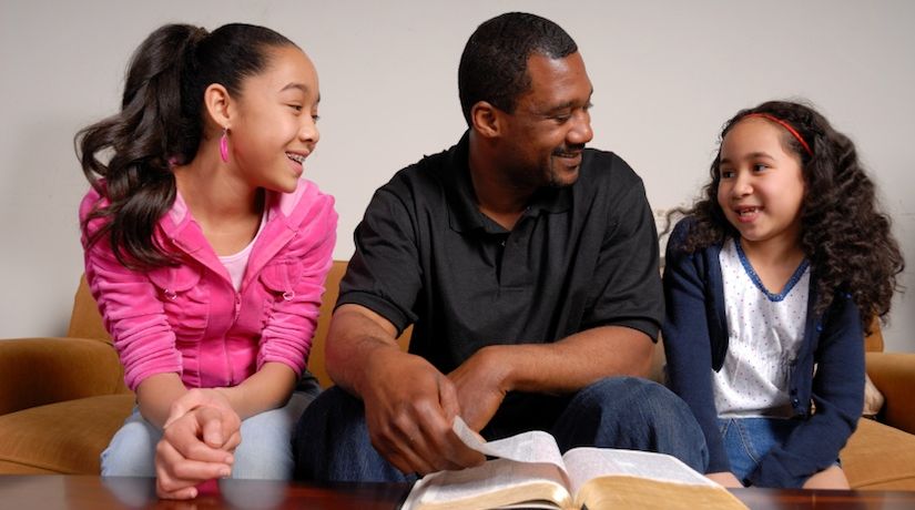 Photo of a father and two daughters with a Bible to illustrate the article Family Bible Study Topics