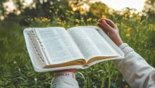 Photo of hands holding a open Bible in a outdoor setting, for the article How the Kingdom Should Change Our Lives Now