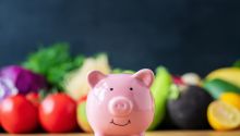 Photo of a piggy bank in front of colorful vegetables to illustrate the article How to Eat Healthy on a Budget