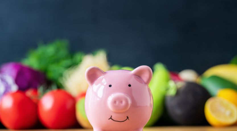 Photo of a piggy bank in front of colorful vegetables to illustrate the article How to Eat Healthy on a Budget