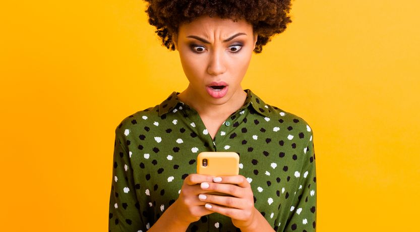 Photo of a woman looking at her phone with a shocked expression to illustrate the article How to Stop Doomscrolling