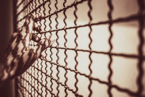 Hands on a wire-mesh prison enclosure to illustrate the article Is Purgatory Biblical?