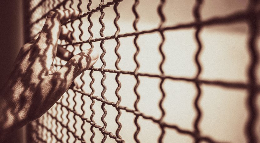 Hands on a wire-mesh prison enclosure to illustrate the article Is Purgatory Biblical?