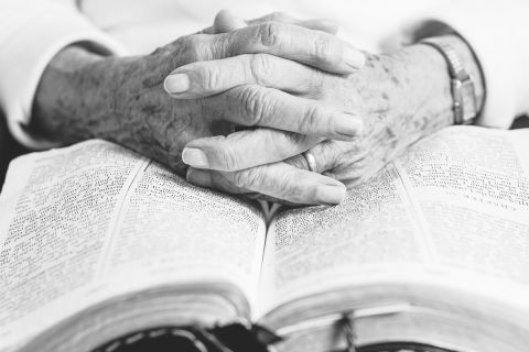 Older person's hands folded on a Bible to illustrate the Legacy of Older Christians