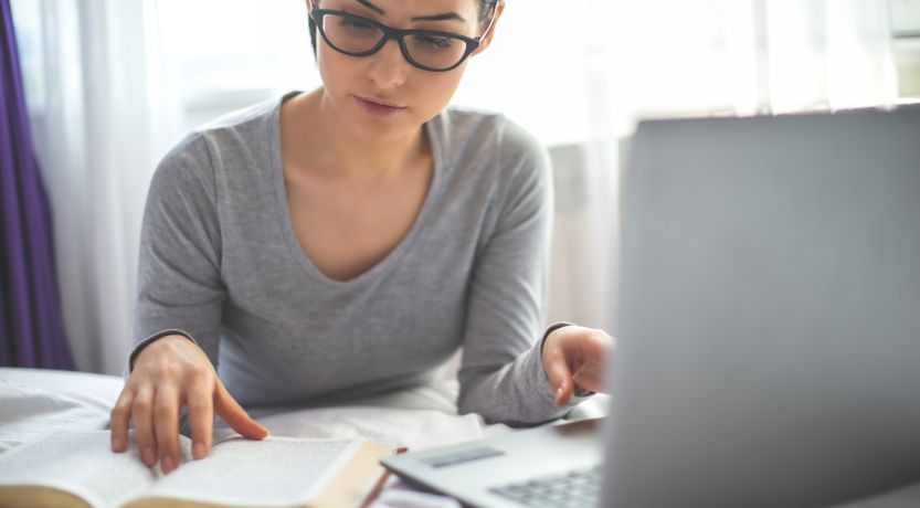 Photo of a woman reading a Bible in front of a computer to illustrate the article The Best Bible Study Tools Online