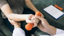 Photo of person lifting a small weight with a physical therapist to illustrate the article “The Spirit Is Willing, but the Flesh Is Weak”