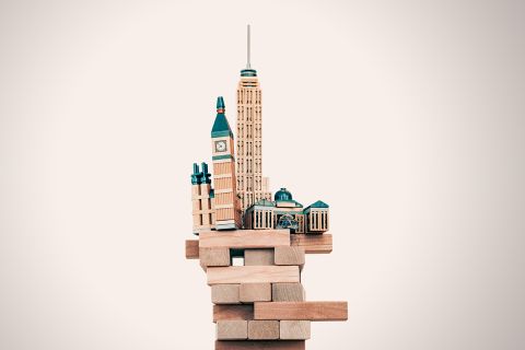Graphic of toy buildings balanced precariously on building blocks to illustrate the article What Can the Righteous Do as the Foundations of Society Are Destroyed?