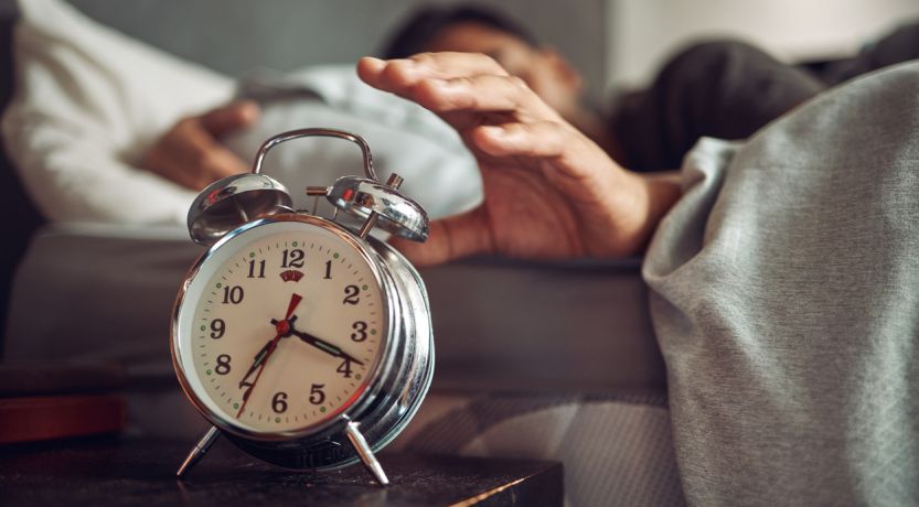 Photo of a man in bed reaching for his alarm clock to illustrate the article 