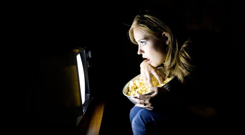 Photo of a girl in a dark room leaning toward a screen with a shocked look on her face to illustrate the article What Does the Bible Say About Watching Bad Things?