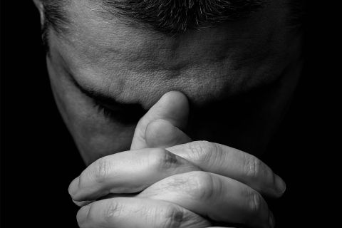 Photo of a man's face with his hands clasped in front of him in prayer, to illustrate the article Why Pray?