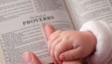 Wisdom Literature in the Bible: photo of hands of an adult and child on the book of Proverbs