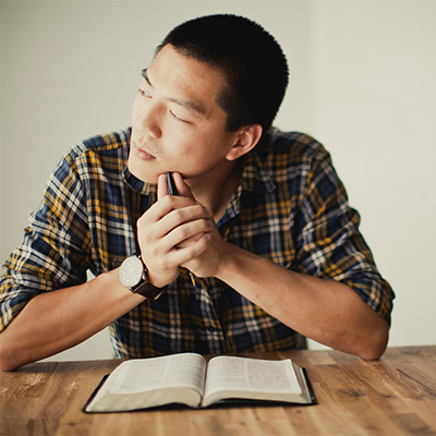 Man sitting at a desk with a Bible in front of him looking to the side with a contemplating gaze