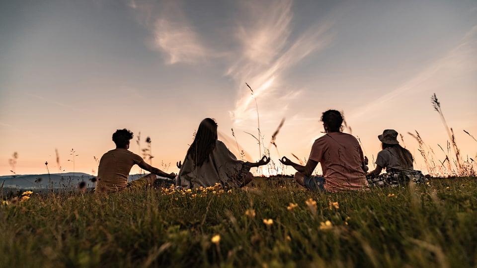 Photo of people sitting in a field facing the sun to illustrate the article Is the Law of Attraction Biblical?