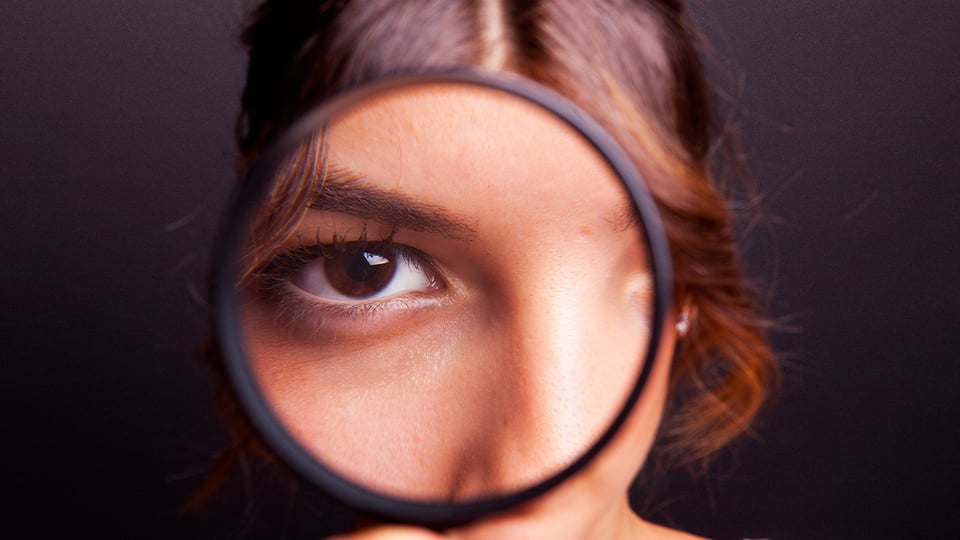 Photo of a girl looking through a magnifying glass at the camera, to illustrate the article Why We Need Spiritual Discernment Now More Than Ever