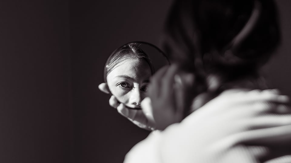 Dark photo of a girl's face reflected in a small round mirror to illustrate the article 