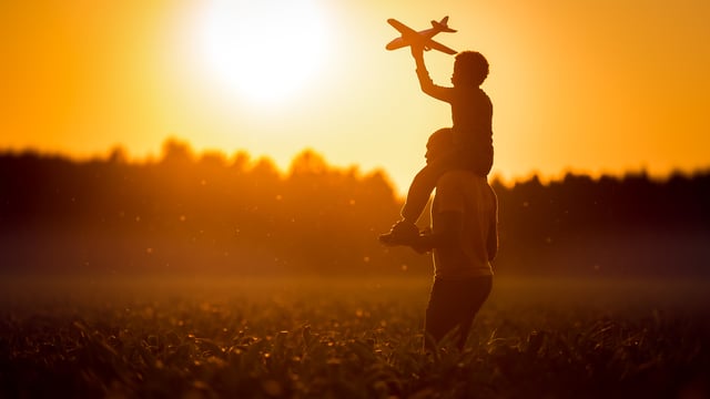 Silhouette of a son on his father's shoulders with a toy airplane to illustrate the article What Brings God Joy?