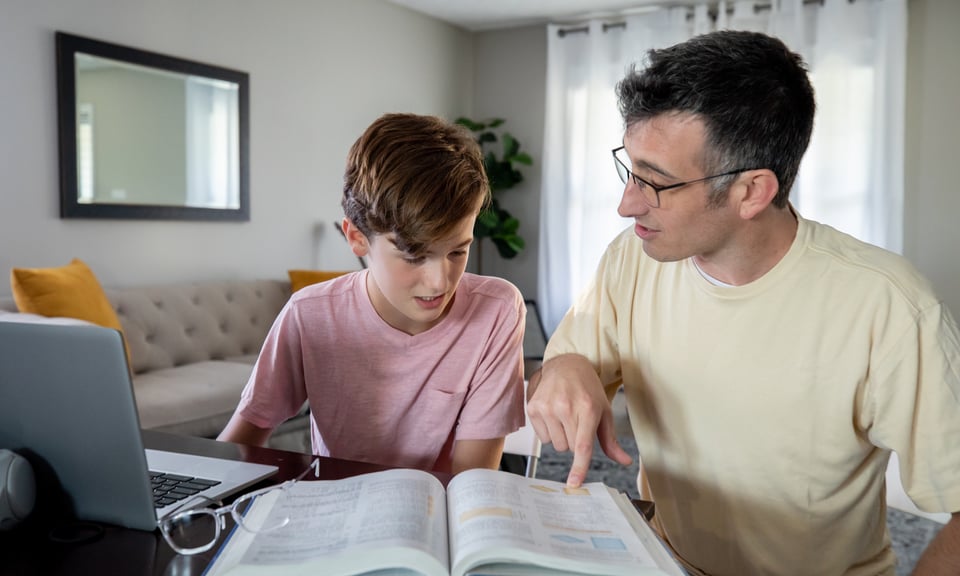 Photo of a son and father looking at a textbook to illustrate the article 